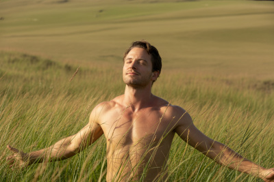 Ein Mann steht mit ausgebreiteten Armen glücklich auf einer Wiese